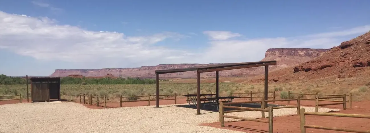 Superbowl group site shad structure and vault toilet with scenic red sandstone cliffs in background.